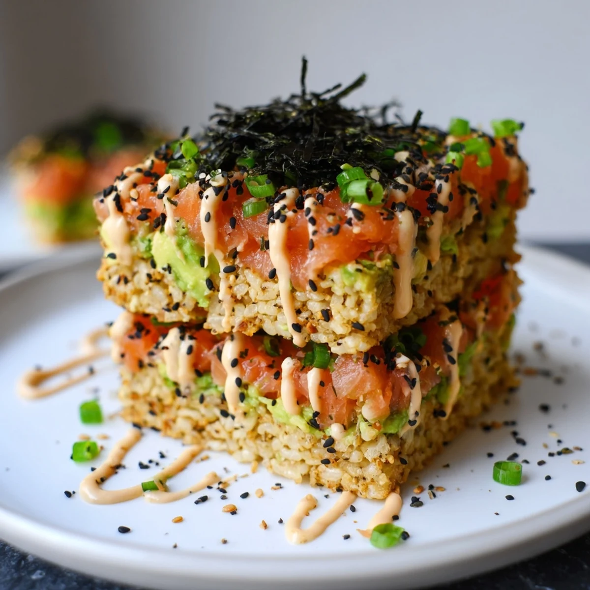 Golden, crispy rice salmon stack featuring fresh salmon, creamy avocado, and spicy mayo drizzle.