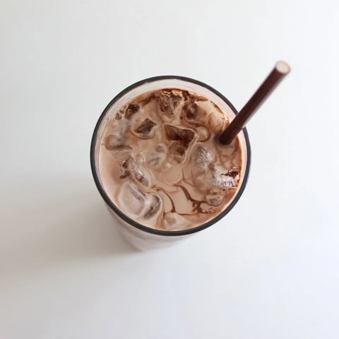 A glass of homemade Milo Ice Latte Hack with ice cubes, creamy milk swirl, and a straw, perfect for a refreshing treat.  
