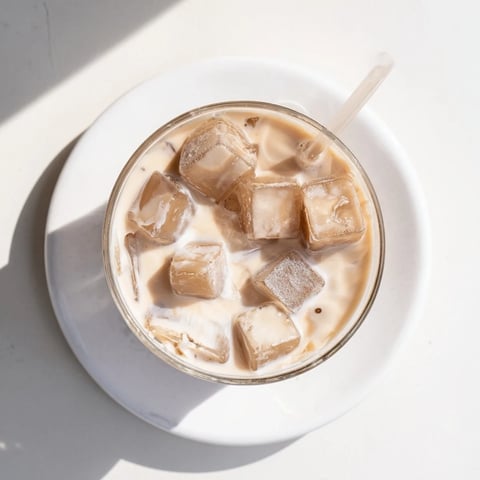 Chilled coffee jelly cubes glistening in creamy milk with ice, served in a clear glass for a refreshing drink.  