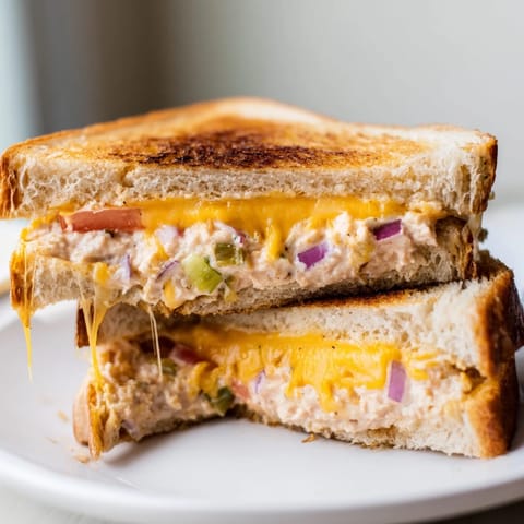 Spicy Tuna Melt on buttery sourdough bread with gooey cheese and a zesty tuna salad, cut diagonally for easy serving.  