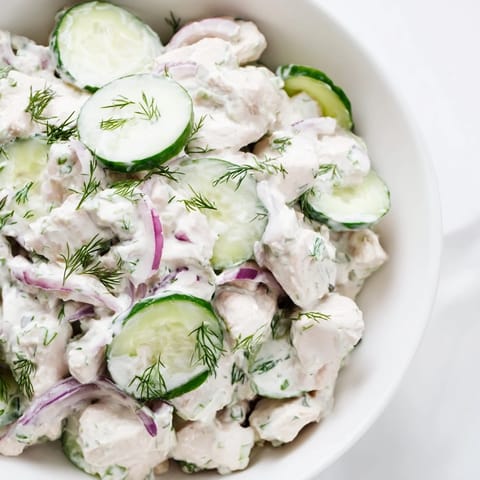 Creamy cucumber chicken salad garnished with green onions and dill, featuring Greek yogurt dressing and colorful vegetables on a rustic wooden table.  