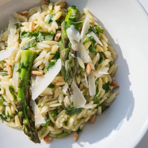 Spoonful of Asparagus Lemon Orzo Salad lifted high, revealing tender grains, greens, and toasted pine nuts.