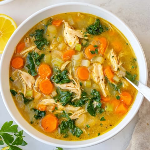 A bowl of High Protein Lemon and Turmeric Chicken Soup garnished with lemon wedges and herbs, ready to serve with crusty bread.