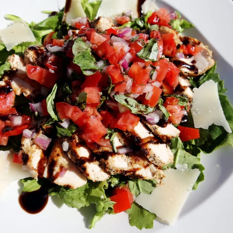 Bruschetta Chicken Salad plated with shaved Parmesan and lemon wedges, showcasing a vibrant mix of greens, grilled chicken, and a colorful tomato topping.