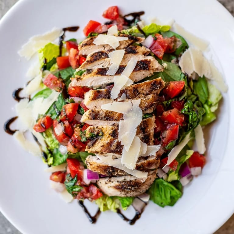 A close-up of Bruschetta Chicken Salad featuring tender chicken breast, diced tomatoes, fresh basil, and a light balsamic glaze on vibrant salad greens.