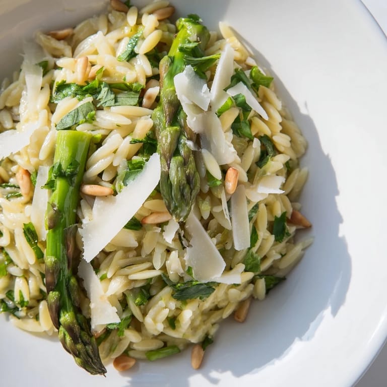 Spoonful of Asparagus Lemon Orzo Salad lifted high, revealing tender grains, greens, and toasted pine nuts.