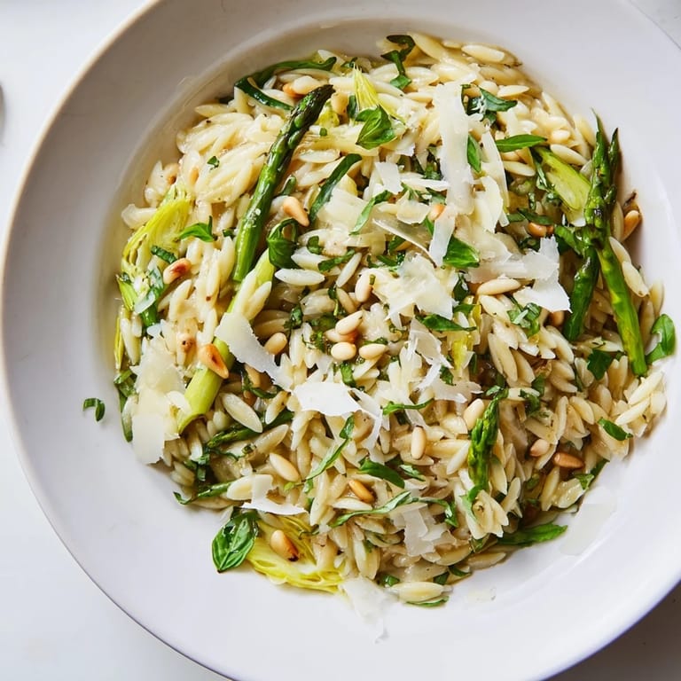 Close-up of Asparagus Lemon Orzo Salad topped with extra Parmesan, fresh herbs, and lemon zest on a marble surface.