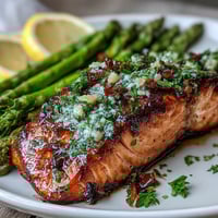 Garlic butter salmon fillets with vibrant asparagus and lemon slices in a sizzling skillet.